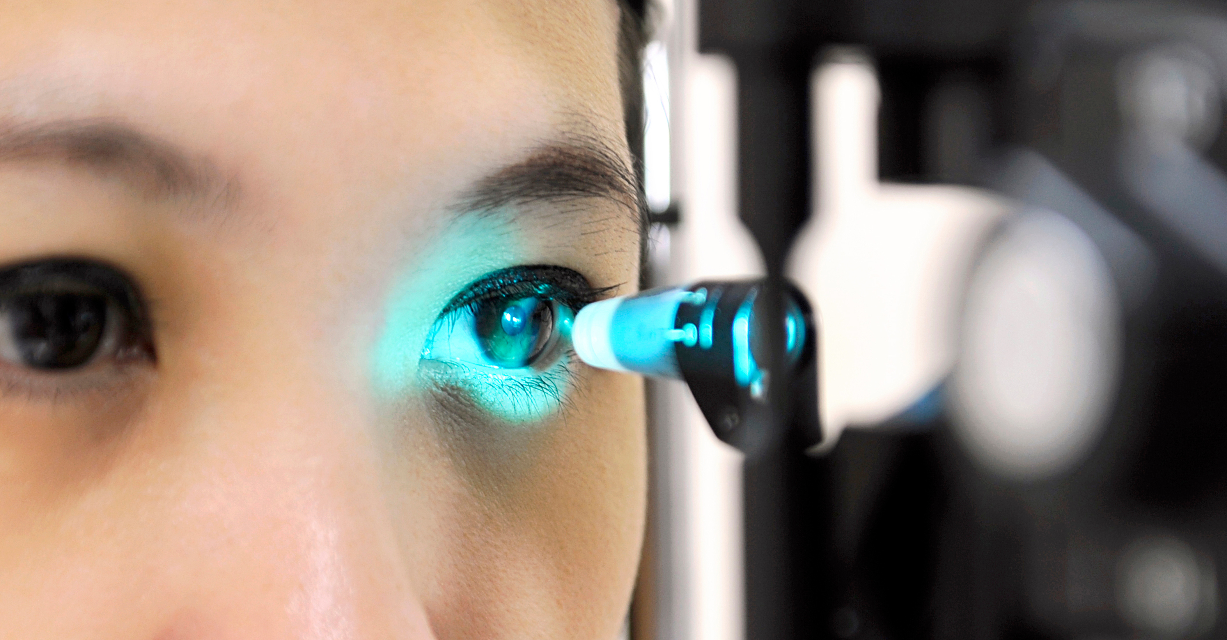 Nahaufnahme einer Patientin bei einer Augenuntersuchung mit einer Spaltlampe und blauem Untersuchungslicht.
