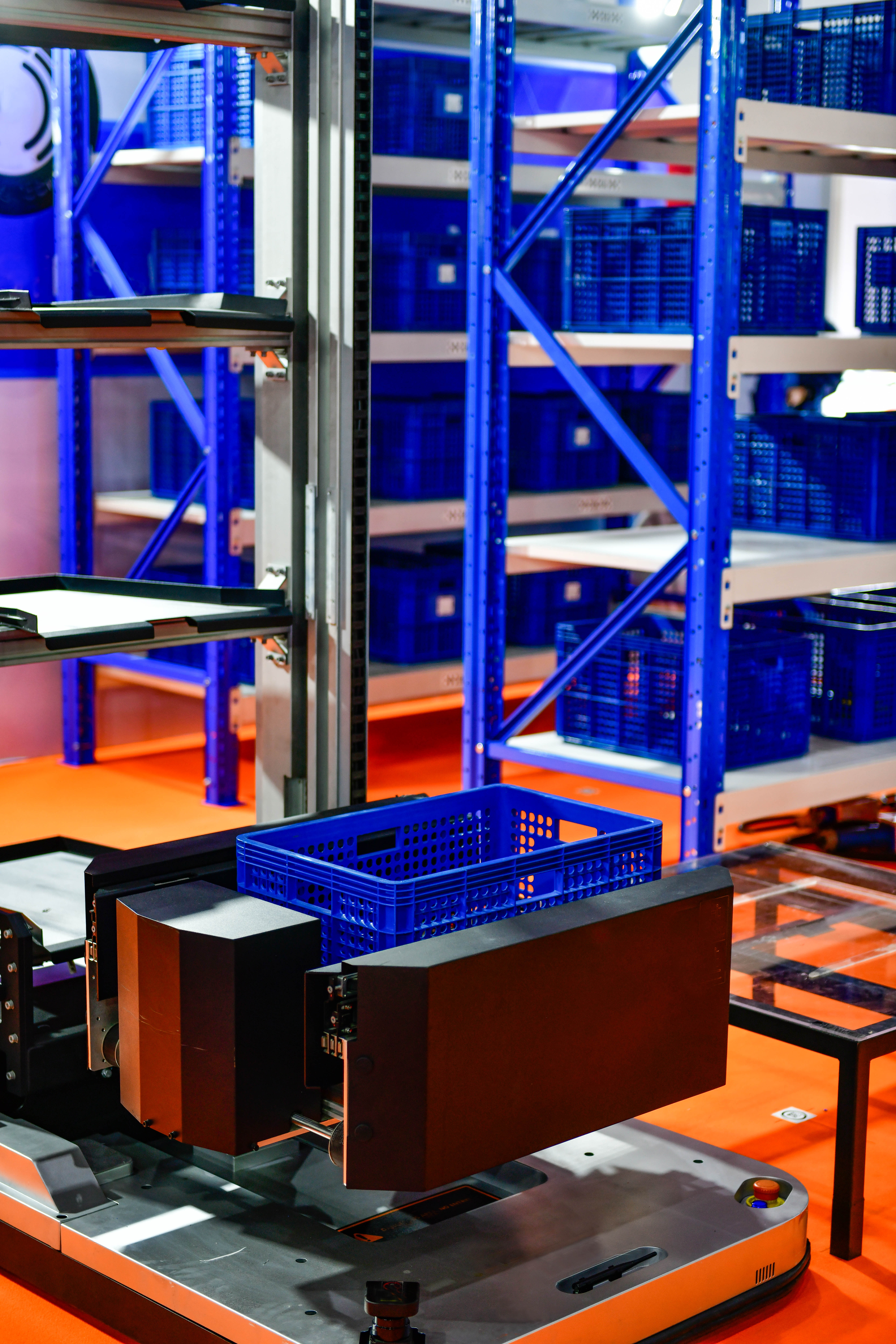 Autonomes Transportsystem mit blauer Kunststoffbox in einem automatisierten Lager mit Hochregalen und weiteren Lagerbehältern.