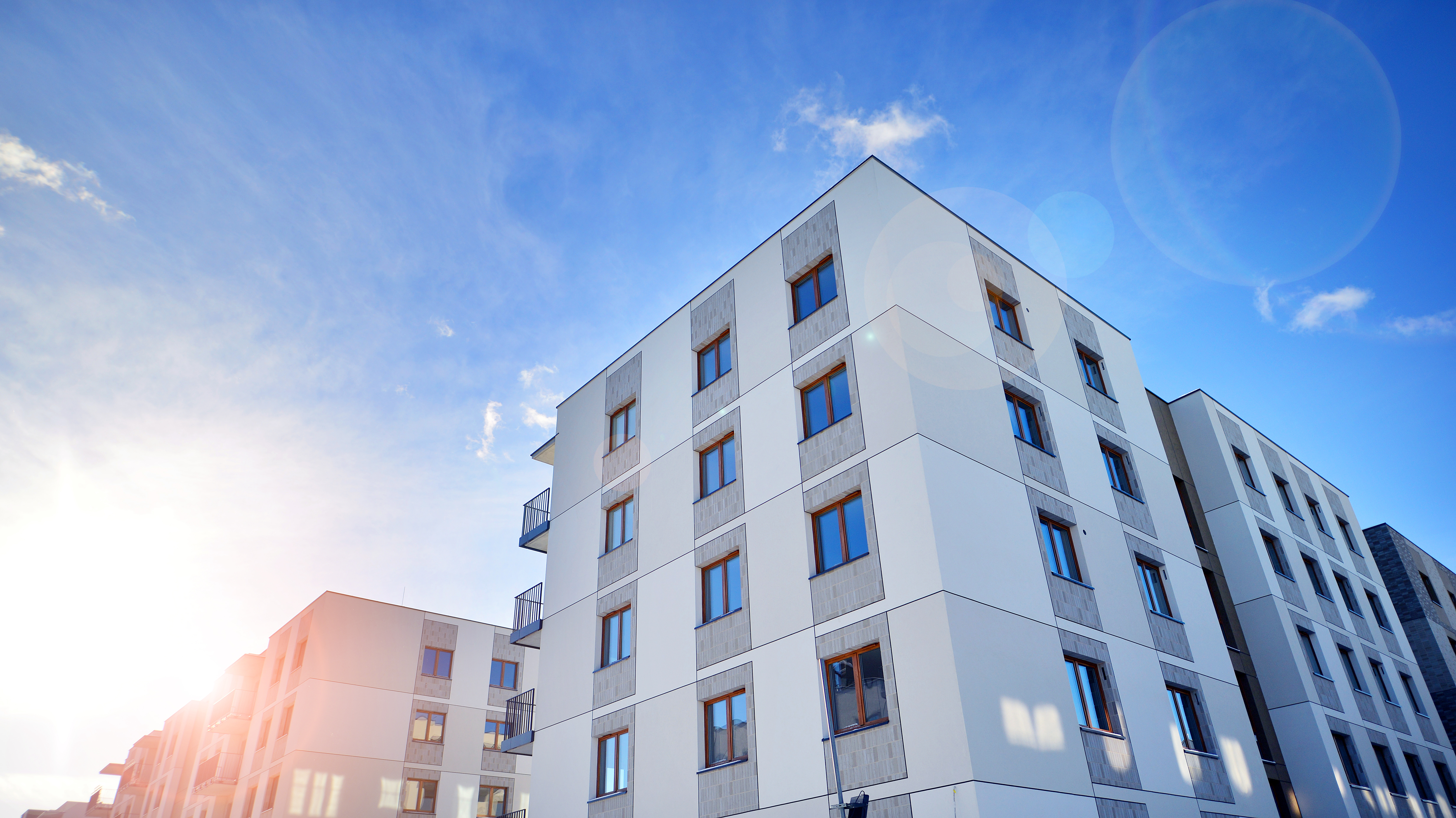 Moderne mehrgeschossige Wohngebäude mit weißen Fassaden, großen Fenstern und Balkonen unter einem blauen Himmel.