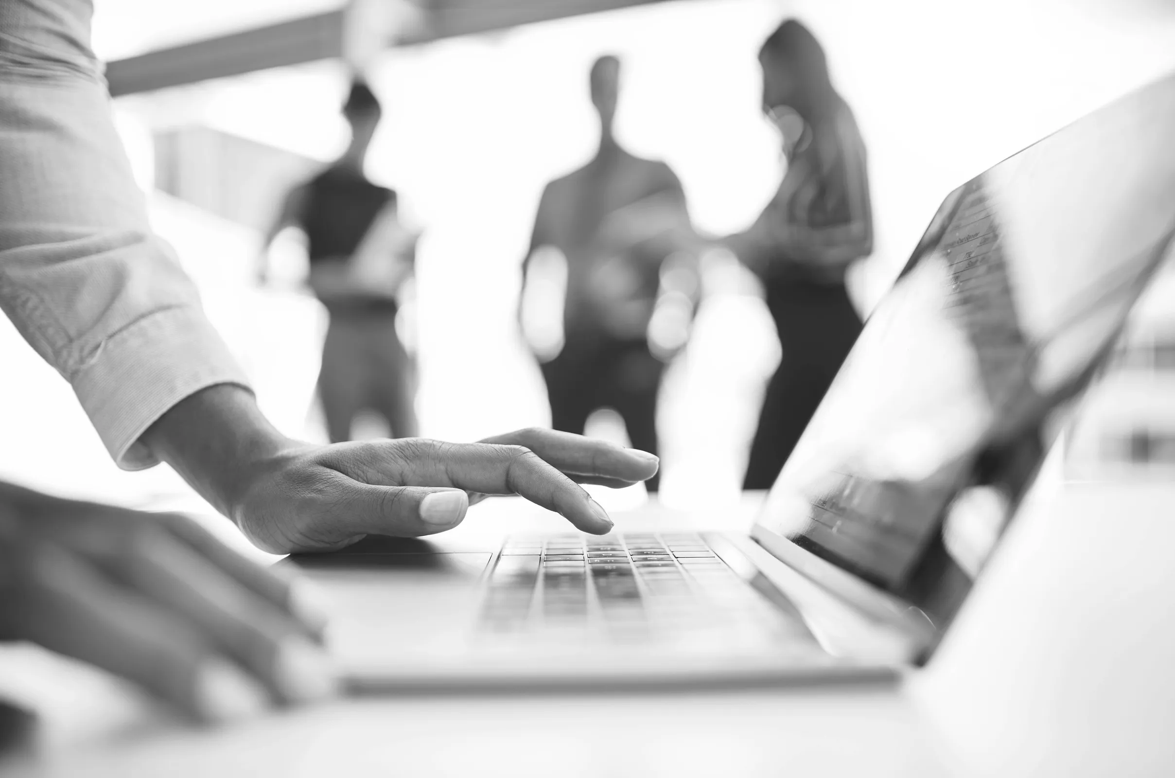 Hands typing on laptop computer with business people in background