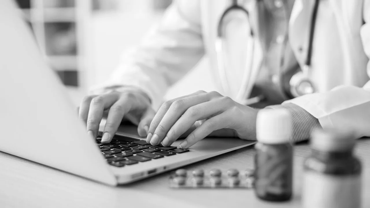 Doctor typing on laptop keyboard with medicines in foreground