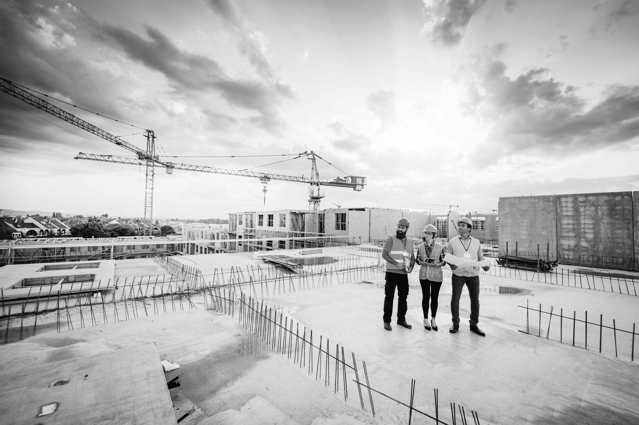 Drei Personen auf Baustelle mit Kränen im Hintergrund